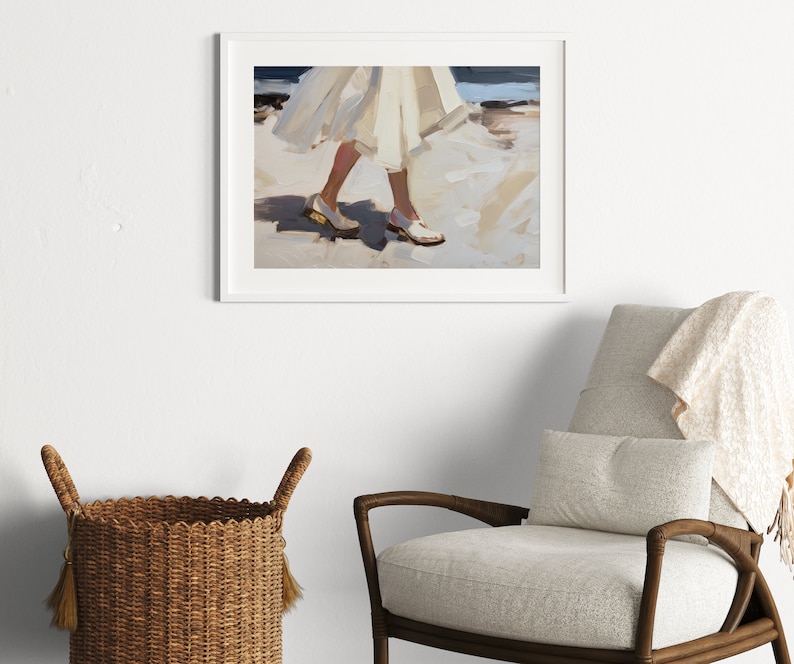 May include: An abstract art print in a white frame depicts a person walking on a beach. The painting features a white dress and white shoes with gold accents. The background shows the ocean and sand, with a palette of whites, blues, and tans.