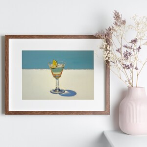 May include: A framed print of a painting depicting a martini glass with a lime wedge on a white surface against a blue background.