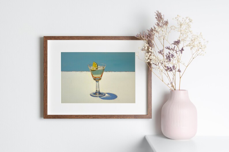 May include: A framed print of a painting depicting a martini glass with a lime wedge on a white surface against a blue background.