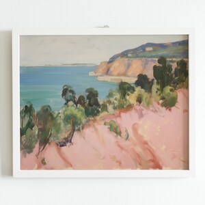 May include: A framed landscape painting featuring a coastal scene with a pink foreground, green trees, a blue ocean, and distant cliffs under a pale sky. The artwork is enclosed in a simple white rectangular frame, displaying visible brushstrokes.