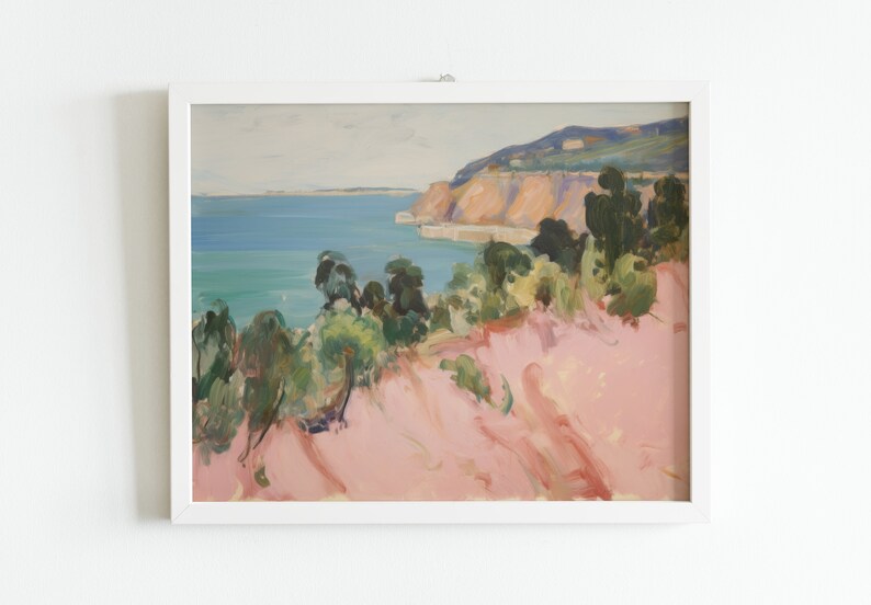 May include: A framed landscape painting featuring a coastal scene with a pink foreground, green trees, a blue ocean, and distant cliffs under a pale sky. The artwork is enclosed in a simple white rectangular frame, displaying visible brushstrokes.