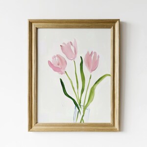 May include: A framed watercolor painting of three pink tulips in a clear glass vase. The tulips are painted in a loose, abstract style with soft, flowing lines. The background is a simple white.