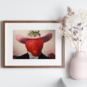 Peut inclure: Une impression d'art encadr&eacute;e repr&eacute;sentant une illustration surr&eacute;aliste d'une grosse fraise rouge portant un chapeau de cow-boy rose et une veste de costume noire avec une chemise blanche &agrave; col et un n&oelig;ud papillon sur fond rose p&acirc;le.