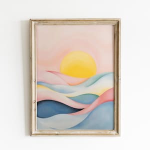 May include: A framed abstract landscape painting. The artwork features a yellow sun setting over rolling hills in shades of pink, blue, and green. The frame is a light, weathered gold color.