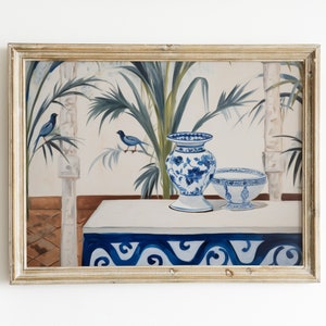 Op de afbeelding: Een ingelijst schilderij met een stilleven met een blauw-witte bloemenvaas en kom op een witte tafel met een blauwe rand. De achtergrond toont palmbladeren en twee blauwe vogels. De lijst is goudkleurig.