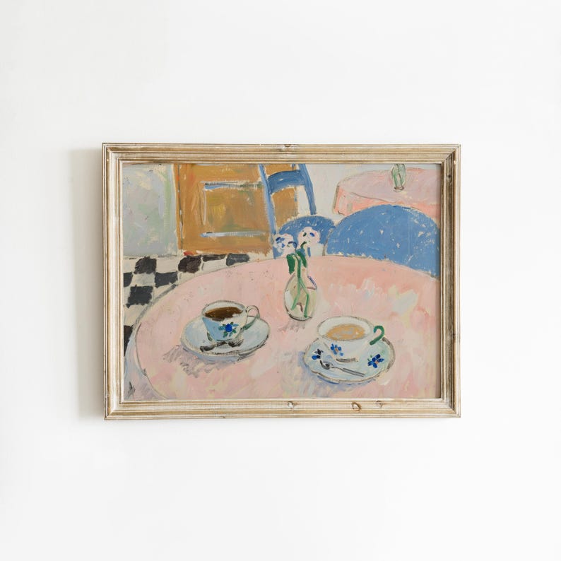 May include: A framed painting depicting a round pink table with two teacups on saucers and a small glass vase with flowers. The scene includes a blue chair, a checkered floor pattern, and a soft color palette of pink, blue, and white brushstrokes.