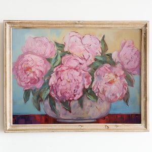 Op de afbeelding: Een ingelijst schilderij van een boeket roze pioenen in een witte vaas. De bloemen zijn in een losse, natuurlijke stijl gerangschikt, en de achtergrond is zacht blauw en geel.