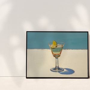 May include: A framed painting of a martini glass with a lime wedge on a white surface against a blue background.