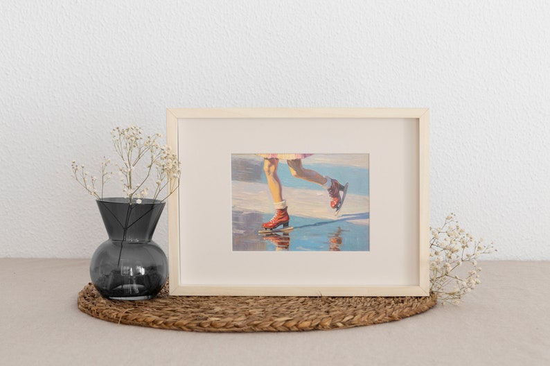 Peut inclure: Un cadre rectangulaire en bois clair contenant une impression d'une peinture repr&eacute;sentant des jambes portant des patins &agrave; glace rouges sur une surface r&eacute;fl&eacute;chissante. Le cadre est plac&eacute; &agrave; c&ocirc;t&eacute; d'un vase en verre gris fonc&eacute; avec des fleurs blanches.