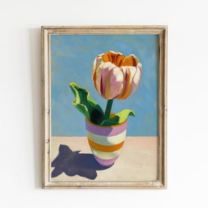 Puede incluir: Un cuadro enmarcado de un tulipán con pétalos rosas, blancos y naranjas en un jarrón a rayas moradas, blancas y naranjas. El fondo es azul claro sólido y la superficie es rosa pálido, con una sombra morada oscura proyectada por el jarrón.