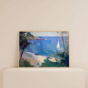 May include: A framed painting of a seascape with sailboats on a blue body of water. The painting is framed in a light wood frame and is set on a white shelf.