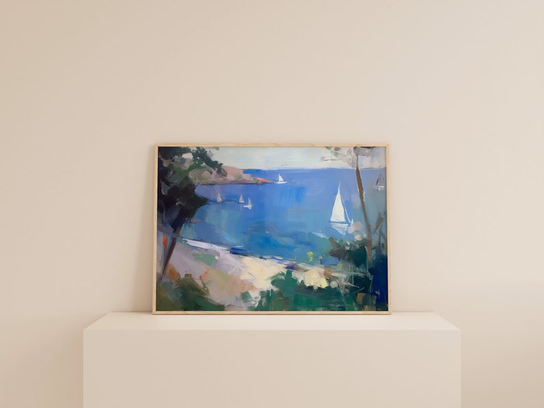 May include: A framed painting of a seascape with sailboats on a blue body of water. The painting is framed in a light wood frame and is set on a white shelf.