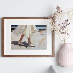May include: A framed art print depicts a person walking on a beach, wearing a white dress and white shoes. The artwork is in a brown frame and is displayed on a white wall. A pink vase with dried flowers sits on a white surface.