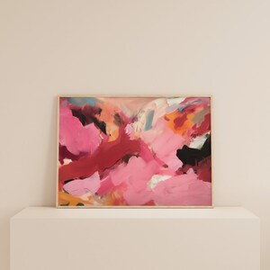May include: Abstract painting with a wooden frame. The artwork features a vibrant mix of pink, red, black, and orange brushstrokes. The painting is displayed on a white surface, creating a modern aesthetic.