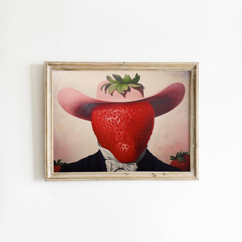 Peut inclure: Une impression d'art encadr&eacute;e repr&eacute;sentant le portrait surr&eacute;aliste d'une grosse fraise rouge portant un chapeau rose &agrave; larges bords et une veste de costume sombre avec une chemise blanche &agrave; col et un n&oelig;ud papillon. Deux fraises sont visibles.