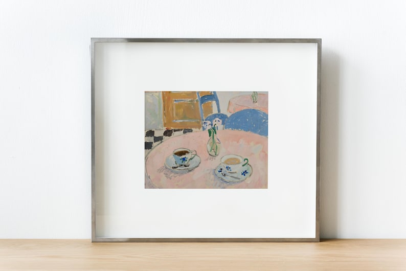May include: A framed print of an oil painting depicting a pink circular table with two teacups on saucers and a small glass vase with flowers. The scene includes a blue chair, a checkered floor, and a wooden cabinet in the background.