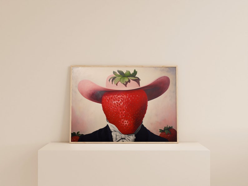 Peut inclure: Une impression d'art encadr&eacute;e repr&eacute;sentant une illustration surr&eacute;aliste d'une grosse fraise rouge portant un chapeau rose &agrave; larges bords et une veste de costume noire avec un n&oelig;ud papillon blanc. Deux petites fraises sont visibles en bas.