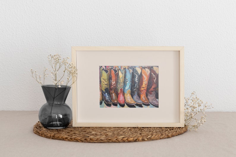 May include: A framed print featuring a row of colorful cowboy boots in shades of yellow, orange, red, blue, black, and brown. The artwork is displayed in a light-colored wooden frame, showcasing a detailed illustration of various boot styles.