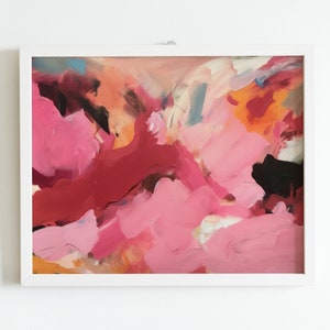 May include: Abstract painting in a white frame. The artwork features a vibrant mix of pink, red, orange, and black brushstrokes. The composition is a dynamic blend of colors and textures, creating a modern aesthetic.