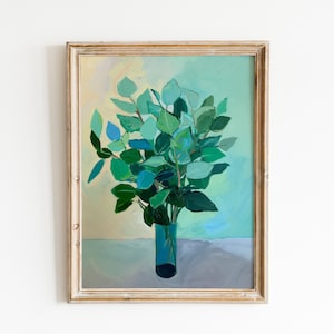Op de afbeelding: Een ingelijst schilderij van een boeket groene bladeren in een blauwe vaas tegen een lichtblauwe en gele achtergrond.