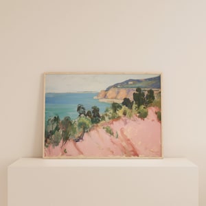 May include: A rectangular landscape painting in a light wood frame depicting a coastal scene. The artwork features a vibrant pink foreground, green trees, a blue ocean, and a distant cliffside under a pale sky, rendered with visible brushstrokes.