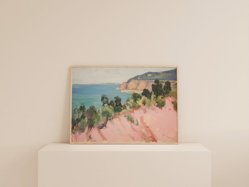 May include: A rectangular landscape painting in a light wood frame depicting a coastal scene. The artwork features a vibrant pink foreground, green trees, a blue ocean, and a distant cliffside under a pale sky, rendered with visible brushstrokes.