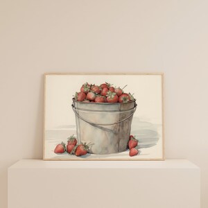 May include: A watercolor painting of a metal bucket filled with red strawberries. The bucket is sitting on a white surface with a few strawberries scattered around it.