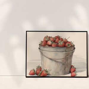 May include: A watercolor painting of a metal bucket filled with red strawberries. The bucket is sitting on a white surface with a few strawberries scattered around it.