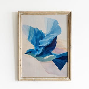 May include: Framed artwork featuring a blue bird in flight. The bird is painted with shades of blue, with wings spread wide. The background is a soft, neutral color, and the frame is a light, distressed wood.