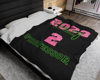 Könnte beinhalten: Schwarze Fleece-Decke mit rosa und grünem Text, der "2023 AKAdemics 2 Professor" lautet.