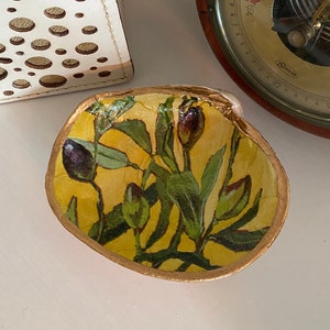 May include: A small, round, gold-rimmed bowl with a floral design. The bowl is filled with a yellow and green floral pattern, featuring small, dark purple flowers. The bowl is sitting on a white surface.