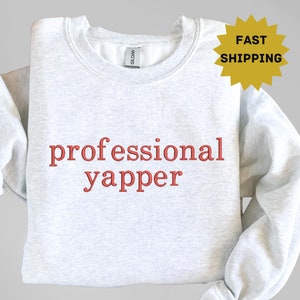 May include: A gray sweatshirt with the text "professional yapper" in red embroidered on the front.