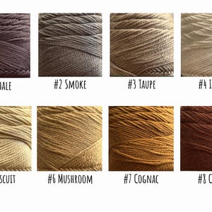 Pode incluir: Um gr&aacute;fico de cores com oito amostras de fios em v&aacute;rias tonalidades. As cores variam do castanho escuro (#1 Shale) ao bege claro (#4 Ivory) e incluem tons de cinza, bege e dourado. Cada amostra &eacute; rotulada com um n&uacute;mero e um nome de cor.