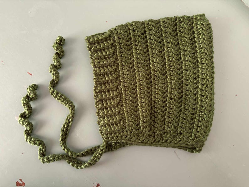 Pode incluir: Touca de croch&ecirc; verde-oliva com la&ccedil;os longos em espiral. A touca apresenta uma textura canelada e &eacute; feita de um fio macio. Este item feito &agrave; m&atilde;o &eacute; perfeito para beb&ecirc;s e crian&ccedil;as pequenas.