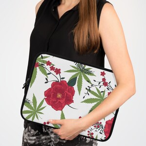 Könnte beinhalten: Eine weiße Laptoptasche mit einem floralen Muster aus roten Blumen und grünen Blättern. Die Tasche hat einen Reißverschluss.