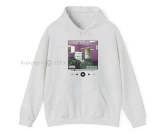 Può includere: Una felpa grigia con una stampa grafica di un edificio viola con il testo "PUMPRULES" e "SUR" su di esso. La grafica include anche un'auto e il testo "THESE ARE THE MIST DAYS OF OUR LIVES".