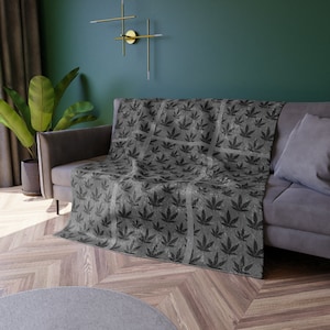 May include: A gray throw blanket with a black leaf pattern. The blanket is draped over a gray couch with a gray pillow.
