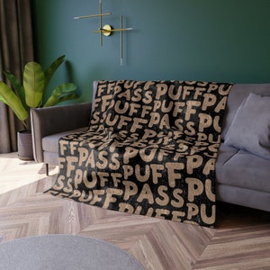May include: Black throw blanket with a repeating pattern of the words "puff" and "pass" in a tan color.
