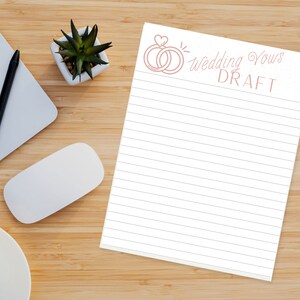 Pode incluir: Um bloco de notas branco com linhas rosa e uma ilustração rosa de dois anéis com um coração no topo. O texto "wedding vows DRAFT" está escrito em itálico rosa.