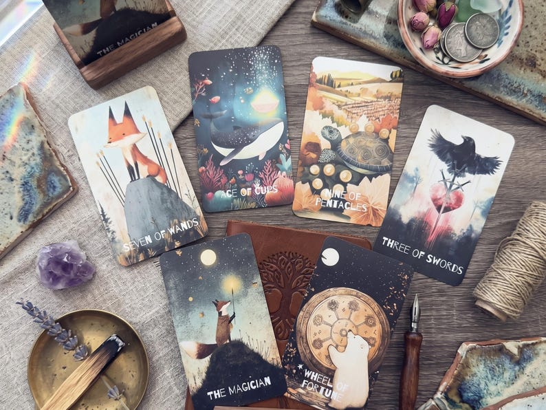 May include: A collection of seven tarot cards featuring illustrated scenes including a fox, a whale, a turtle, a raven, and a polar bear. The cards are labeled Seven of Wands, Ace of Cups, Nine of Pentacles, Three of Swords, The Magician, and Wheel of Fortune.