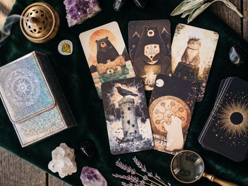 May include: A deck of tarot cards featuring animal illustrations, including a bear on a log, a bear with a campfire, a cat, a raven on a tower labeled The Tower, and a polar bear with a wheel labeled Wheel of Fortune, with a holographic box.