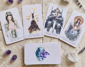 May include: A tarot card deck with four face-up cards and a stack of cards below. The cards feature watercolor illustrations of figures and symbols. The cards are labeled "The Empress", "Six of Wands", "King of Swords", and "Queen of Pentacles".