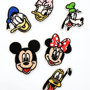Pode incluir: Conjunto de sete patches bordados com personagens de desenhos animados. Inclui Mickey Mouse, Minnie Mouse, Pato Donald, Margarida, Pateta e Pluto. Cada patch tem uma borda preta e cores vibrantes.
