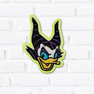 May include: An embroidered patch featuring a stylized duck character with large black horns, a white face, bright blue eyes, and a yellow beak, all outlined with a vibrant neon yellow border against a white brick background.