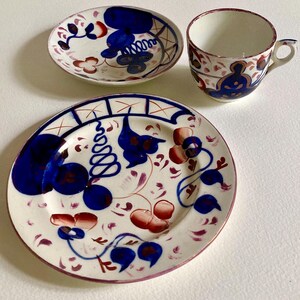 May include: A white ceramic tea set with blue, red, and purple floral designs. The set includes a cup, a saucer, and a plate. The cup has a handle and the plate is approximately 8 inches in diameter.