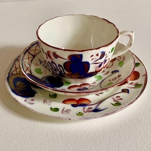 May include: A white teacup and saucer set with a floral design. The cup and saucers have a scalloped edge and are decorated with blue, red, and green floral patterns. The set is likely vintage or antique.