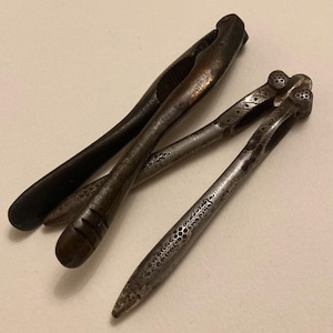 2 vintage nut crackers. 1) Antique nutcracker swings over to crack slightly different sized nuts and has detailed decoration. 2) Bronzed.