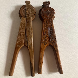 Peut inclure: Deux casse-noix anciens en bois avec des motifs sculptés complexes. Les casse-noix sont de couleur marron chaud, avec des motifs géométriques et floraux détaillés. Les poignées sont incurvées et le dessus a un motif circulaire.