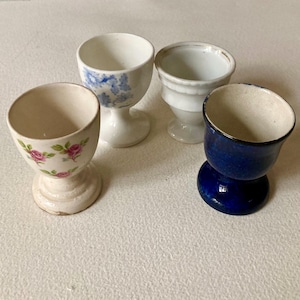Four antique egg cups. Please see photographs and description for condition. Pink roses, dark blue, baby blue & white porcelain, pottery …