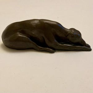 Bronzed resin dog figurine lying down. possibly J. Spouse as impressed intertwined J and s. Green baize on the base. Approx: 6 1/2 inches.